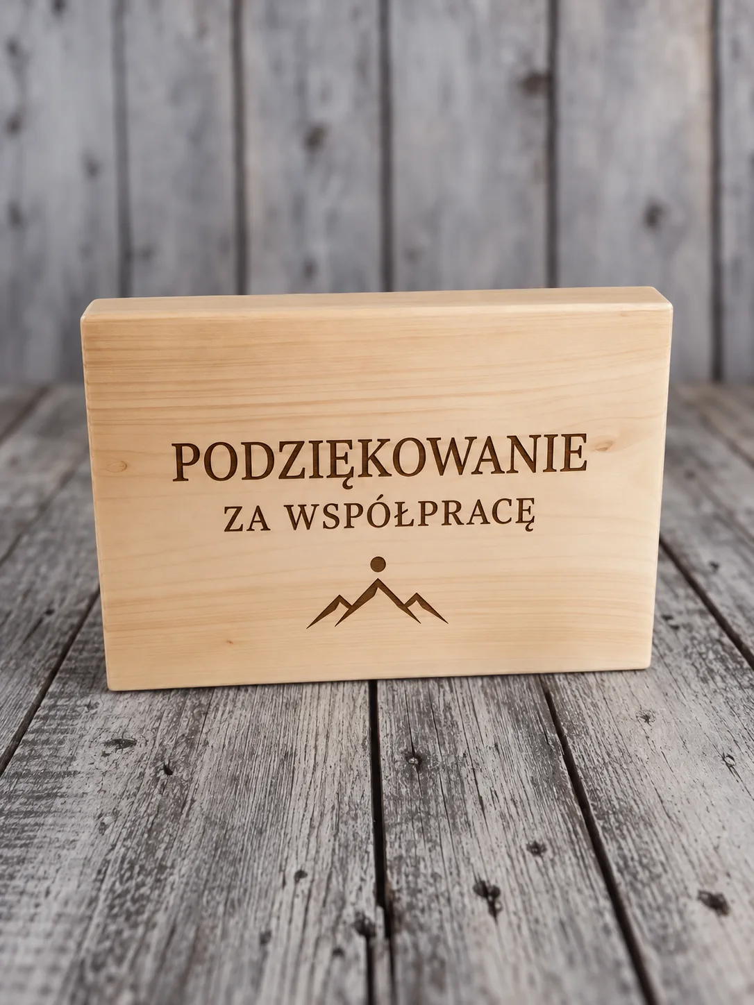 Pudełko z litego drewna z grawerem laserowym napisu i znaku gór na wieku, stojące na szarych, zwietrzałych deskach