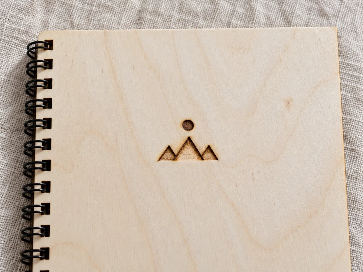 Okładka notesu ze sklejki brzozowej w zbliżeniu, z wypalonym laserowo logo i czarną spiralą przy lewej krawędzi